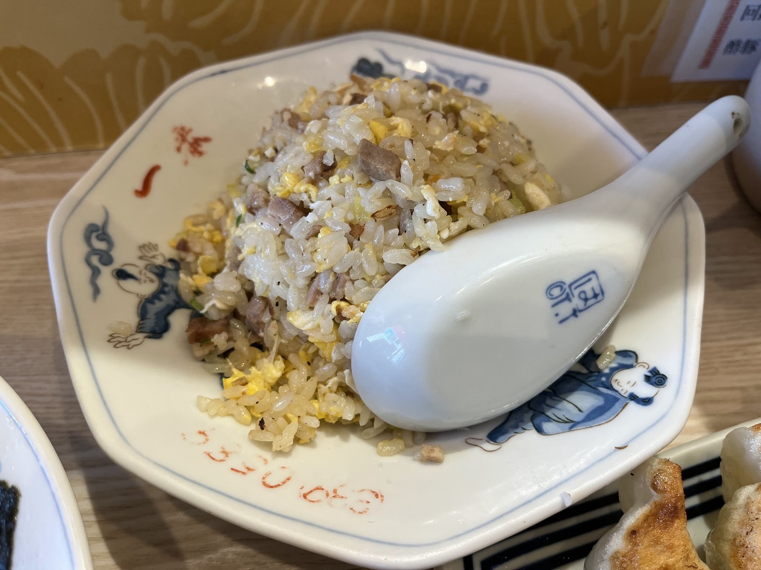 八角形の中華皿に盛られたチャーハンと白いレンゲ、隣に見える餃子の皿